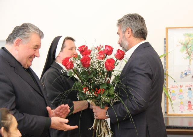 Ing. Tomáš Chrenek předává kytici vedoucí azylového domu sestře Imeldě, za účasti kardinála Dominika Duky